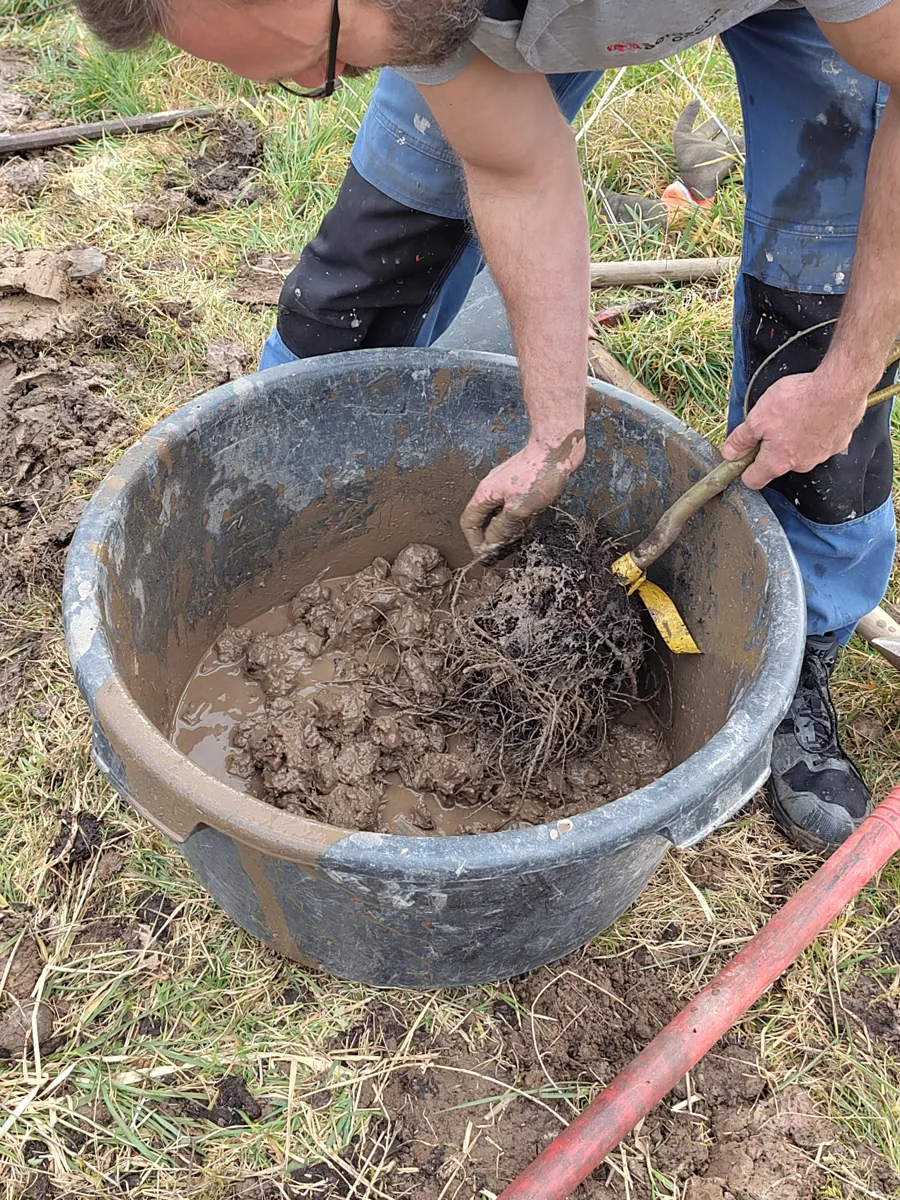 Hands mixing earth and fibres during an outdoor workshop